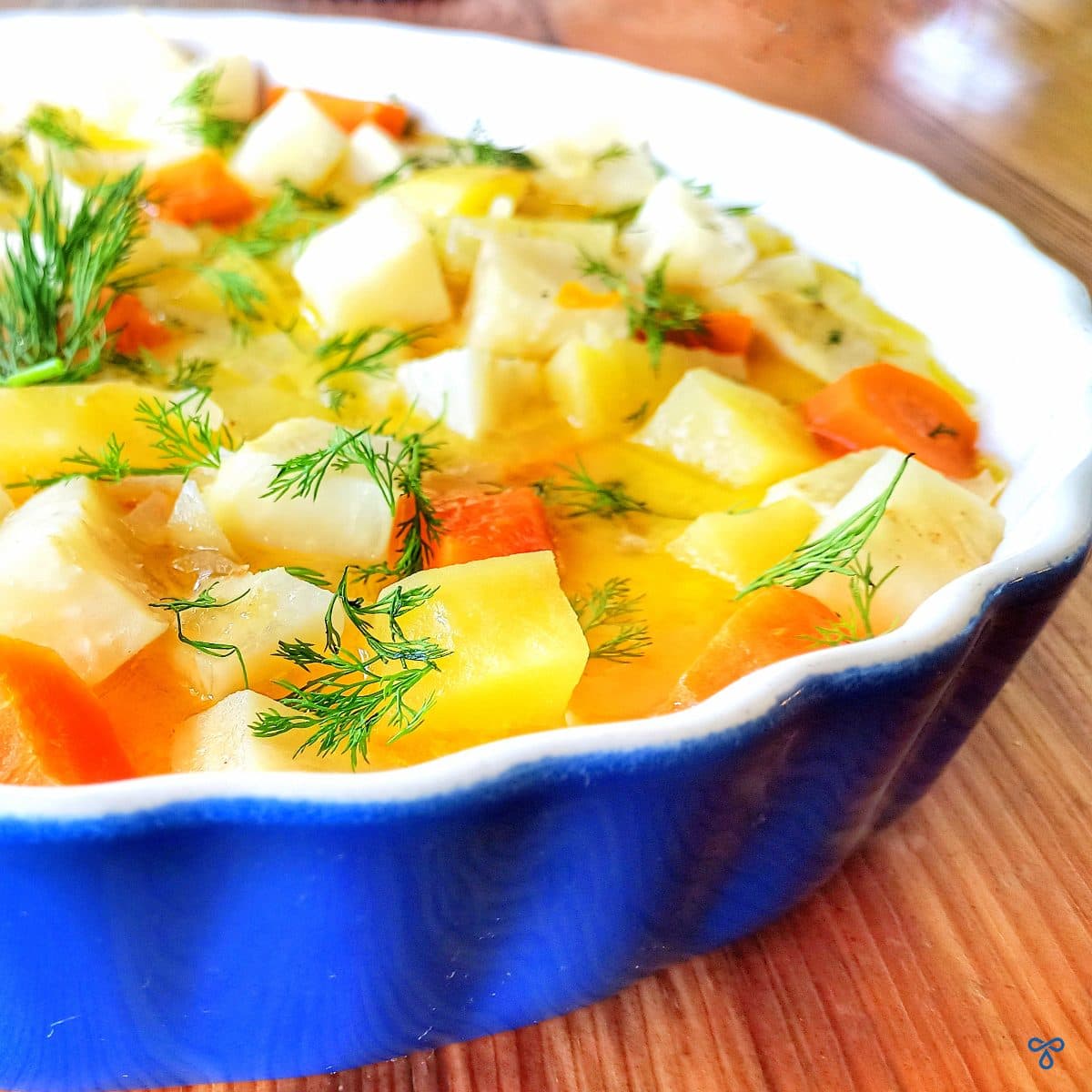 A close up shot of pieces of celeriac, potato & carrot in an olive oil & orange sauce, topped with dill.
