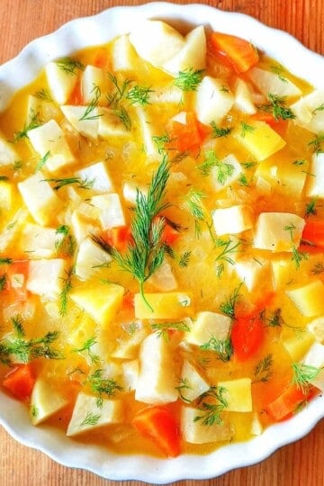 A bowl of celeriac, carrot and potato chunks in an orange sauce with sprinkles of fresh chopped dill over the top.