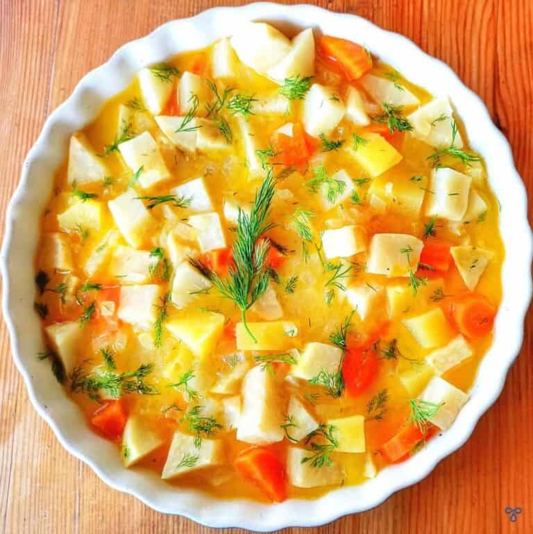 A bowl of celeriac, carrot and potato chunks in an orange sauce with sprinkles of fresh chopped dill over the top.