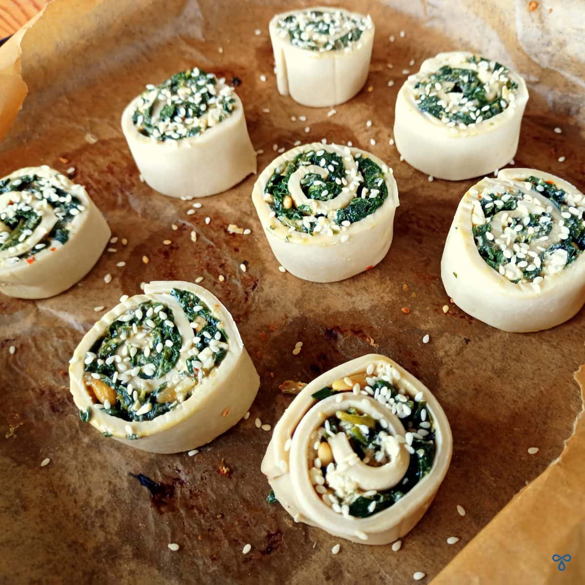 Uncooked pastry pinwheels on greaseproof paper.
