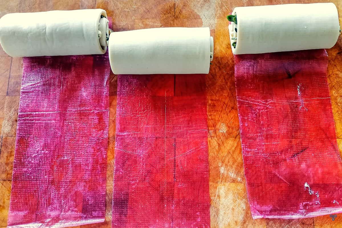 Three rolls of puff pastry on pink cellophane.