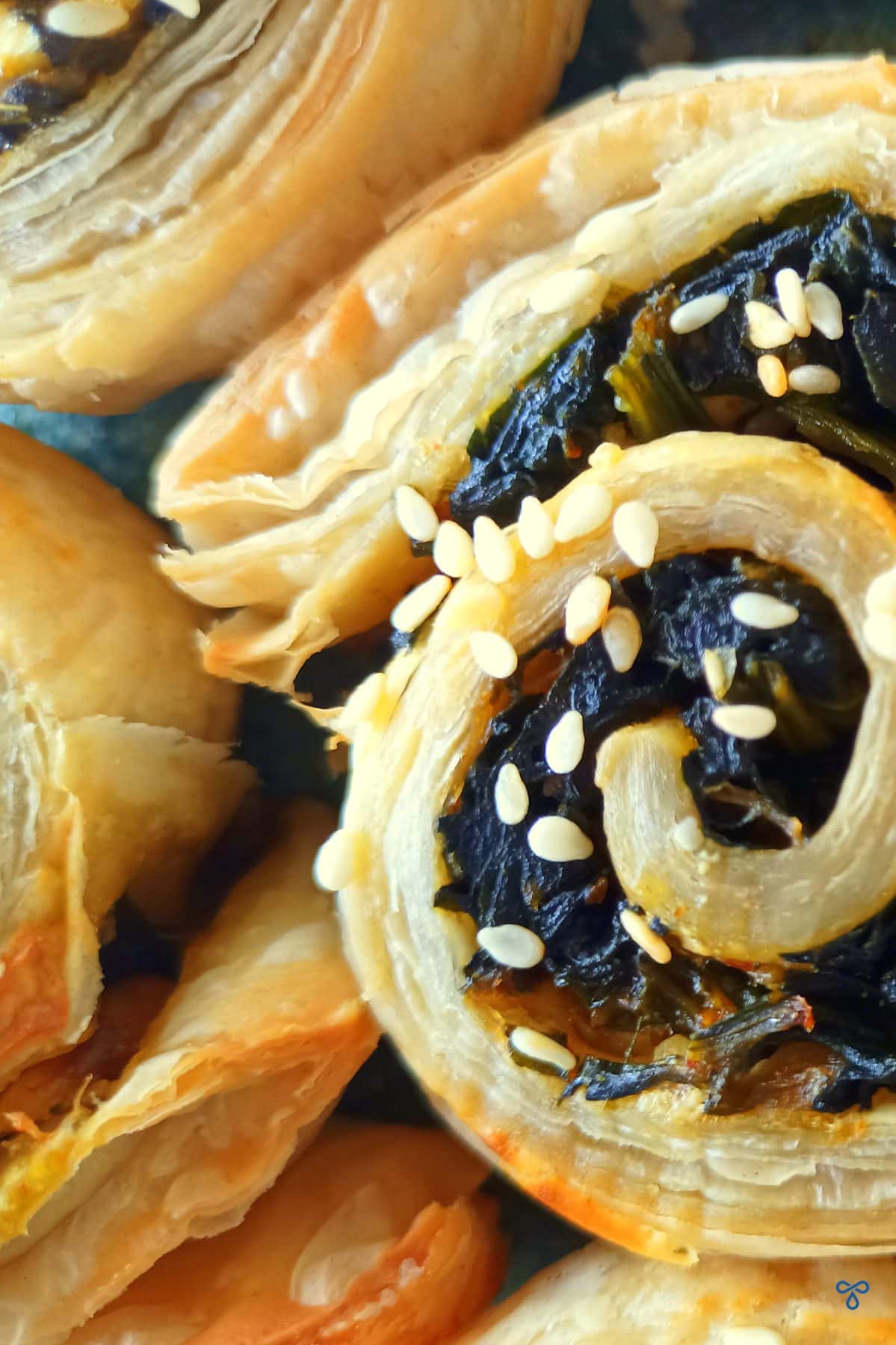 A close up of half of a spinach puff pastry pinwheel topped with sesame seeds.