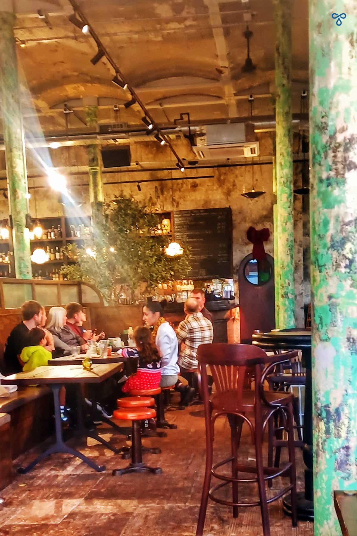Interior of an old Wigan mill made into a pub. People are sitting at round tables and pillars support the stone vaulted ceiling.