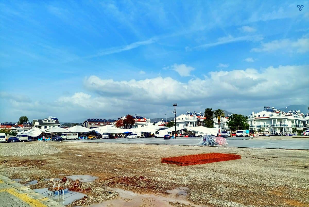 A big gravel space with market stalls around the far edge in the distance.