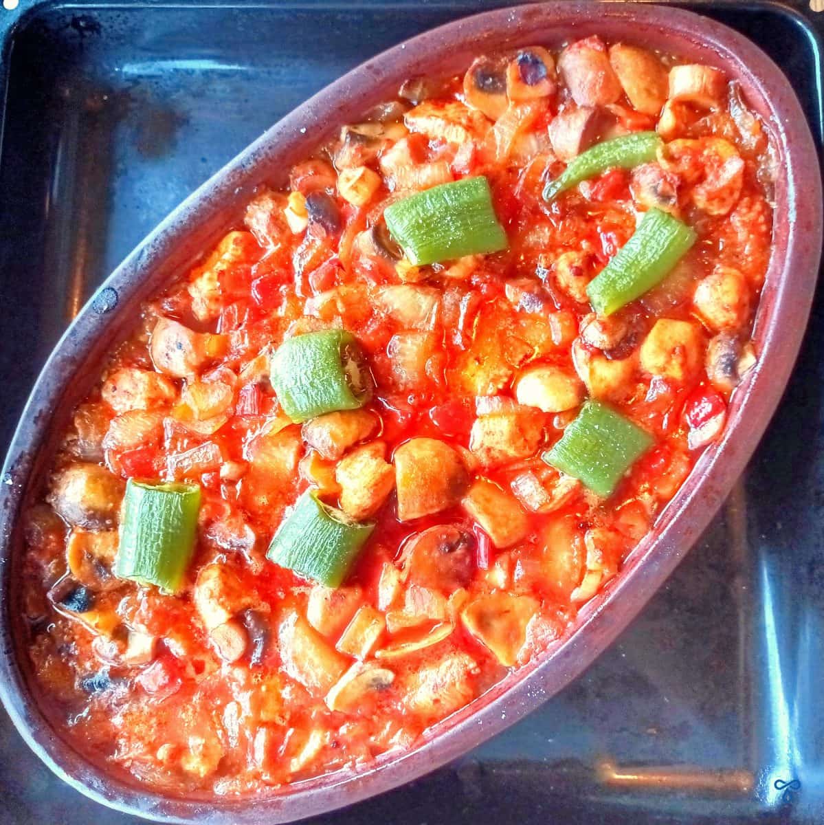 Turkish chicken casserole in a shallow oval-shaped clay pot, topped with chopped green peppers.