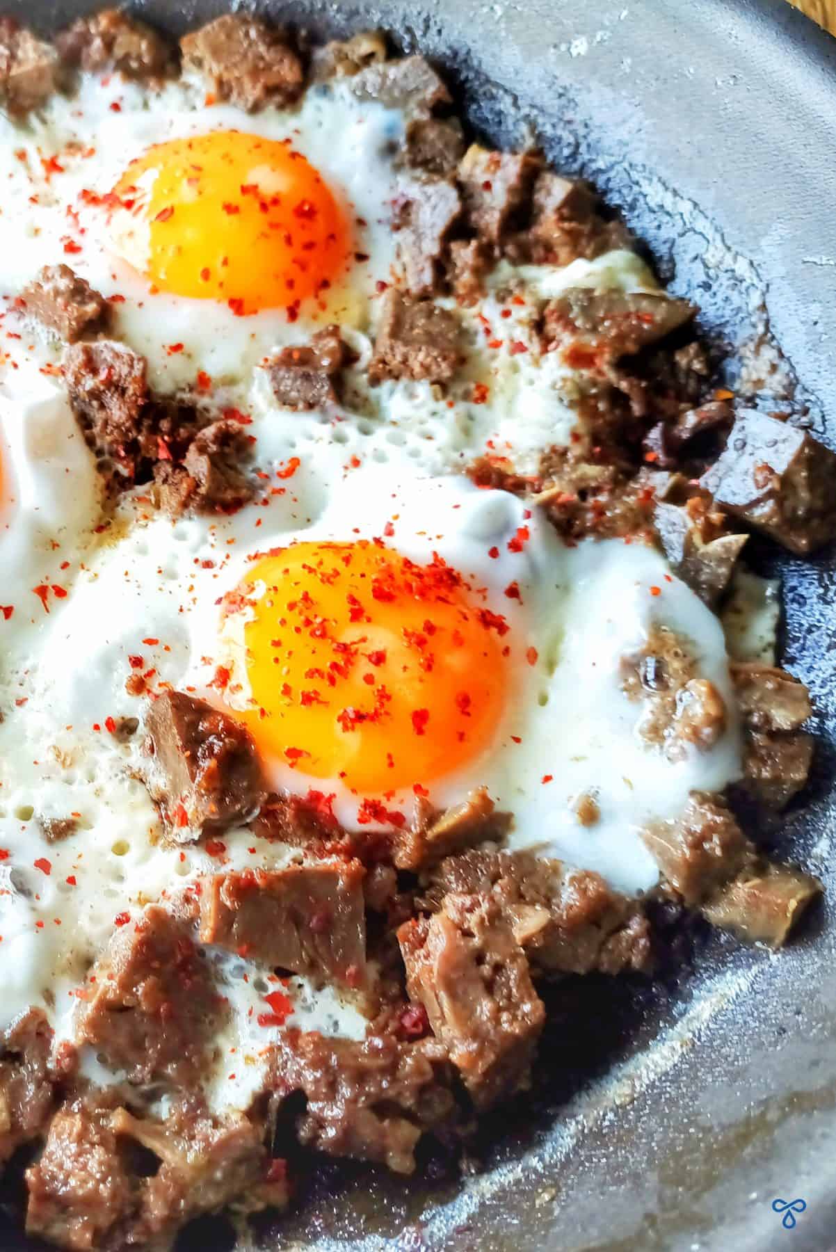 A close up of two eggs cooked with chunks of Turkish kavurma meat.