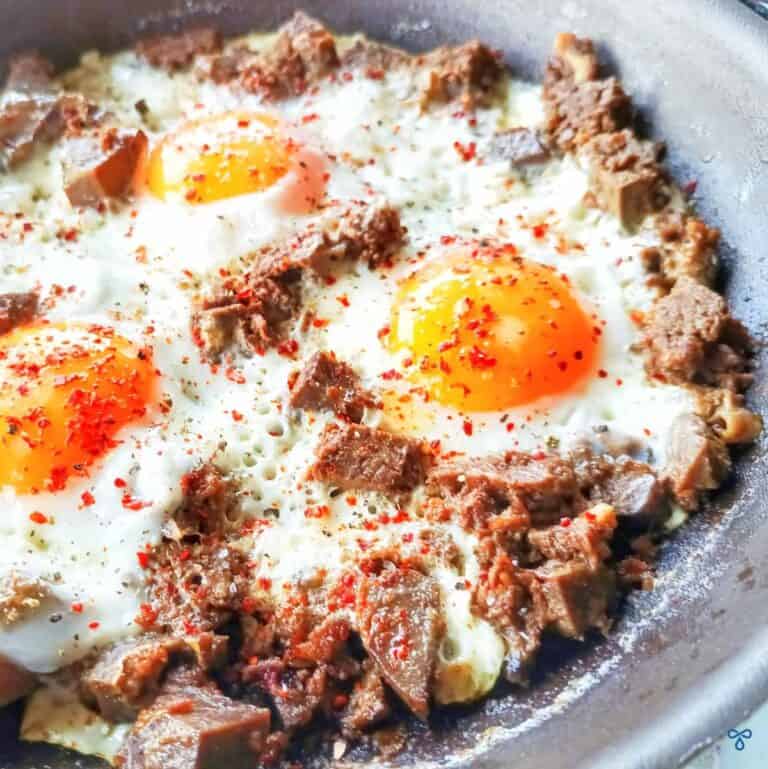 A close up of three fried eggs in a frying pan with chunks of beef scattered through them.