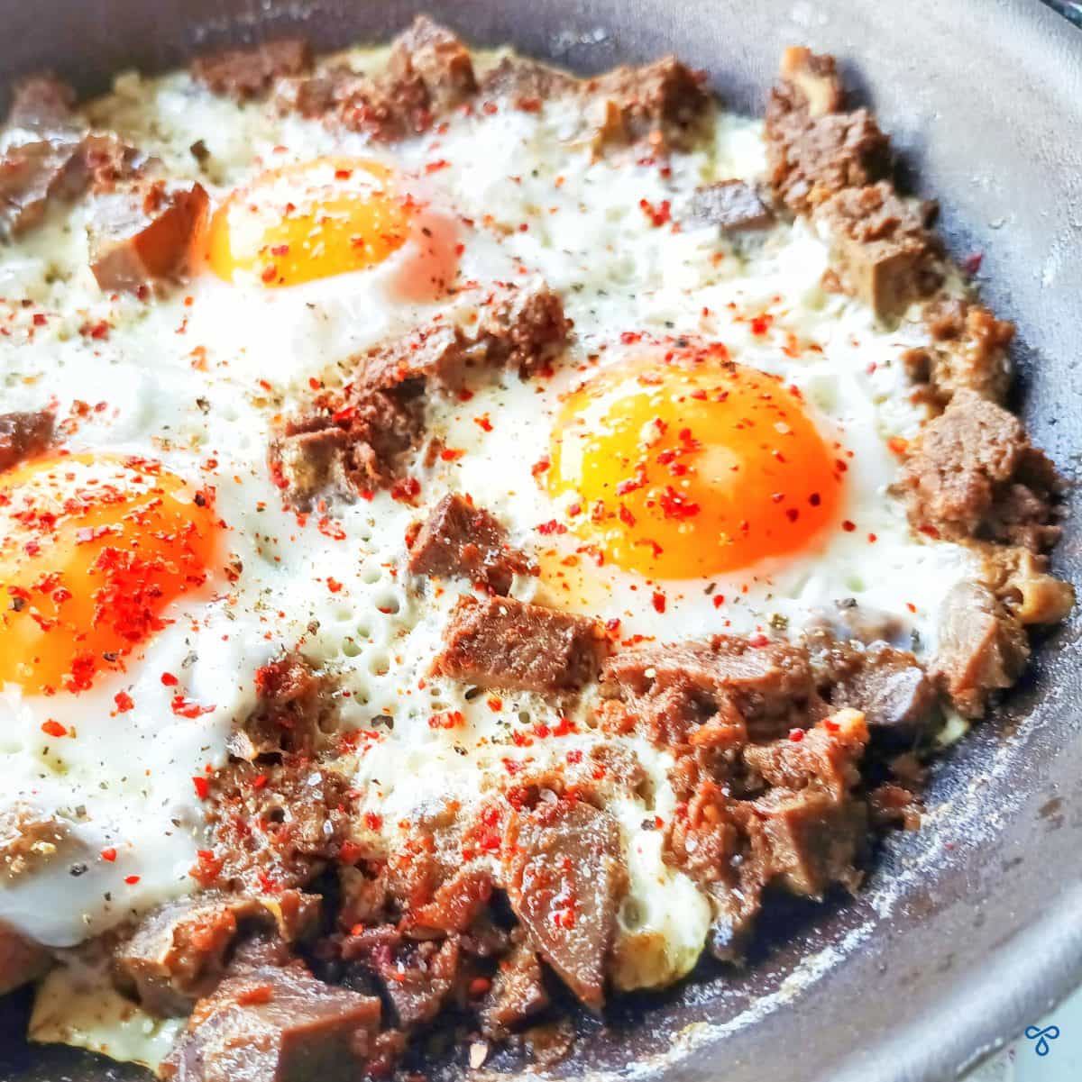 A close up of three fried eggs in a frying pan with chunks of beef scattered through them.