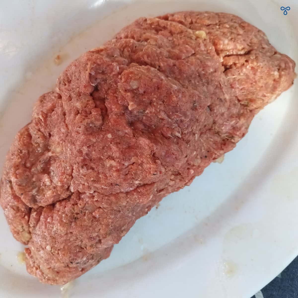 A slab of kneaded minced beef on a white tray.