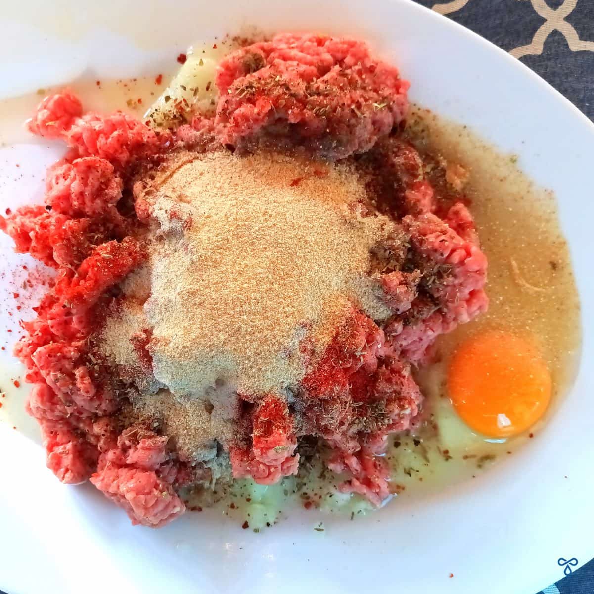 Raw minced beef on a plate, topped with fine bread crumbs and a raw egg.