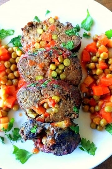 Four slices of Dalyan Köfte - Turkish meatloaf stuffed with vegetables in the middle. Mixed chopped vegetables line the sides of the meatloaf.