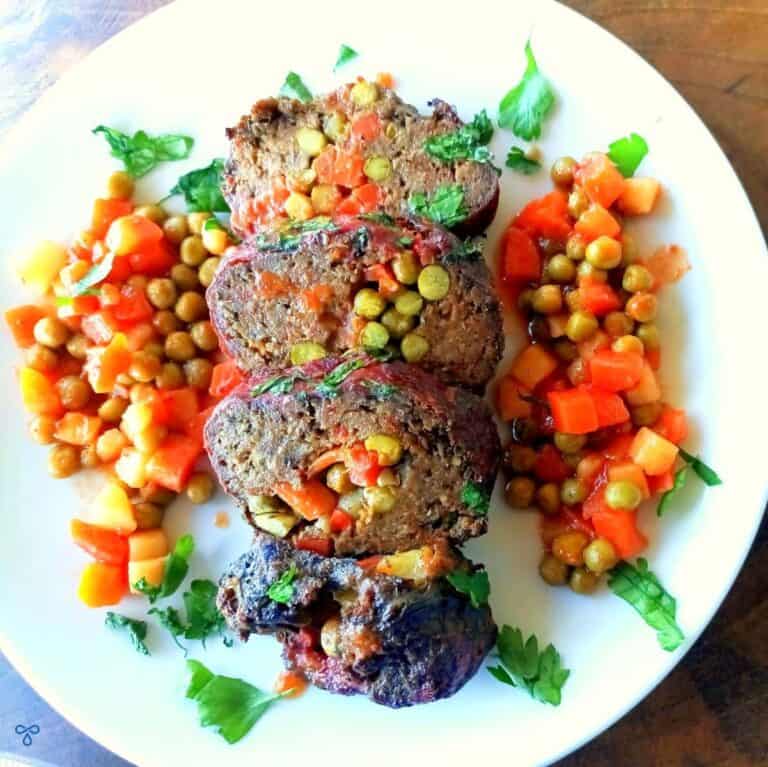 Four slices of Dalyan Köfte - Turkish meatloaf stuffed with vegetables in the middle. Mixed chopped vegetables line the sides of the meatloaf.