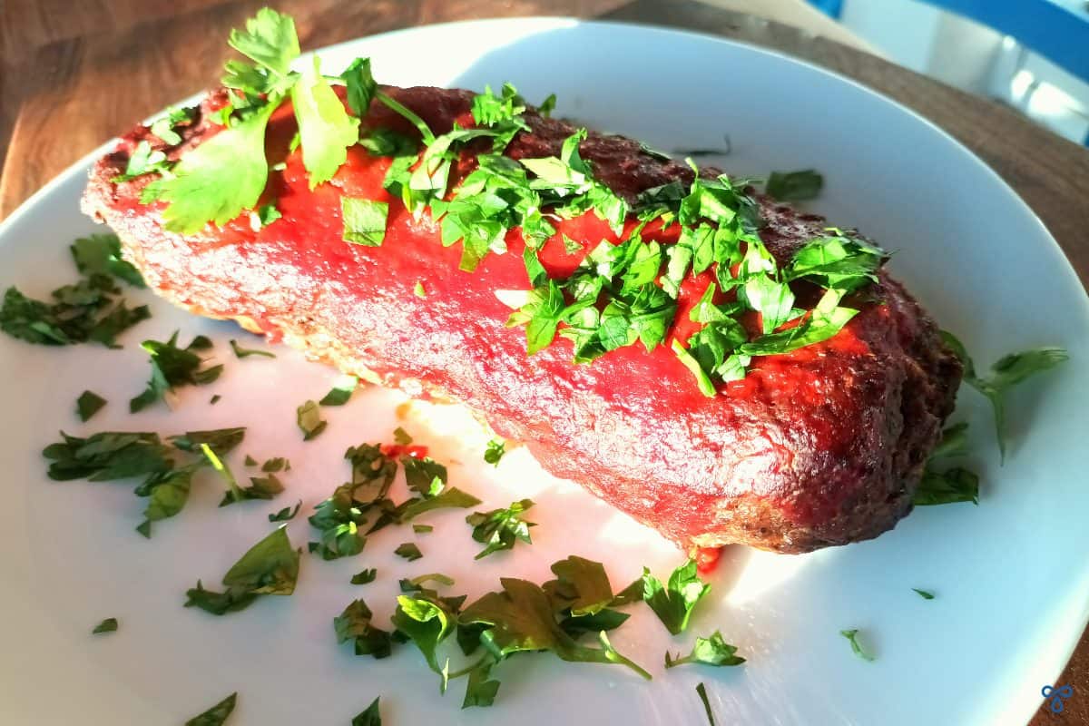 A coated cooked meatloaf topped with chopped parsley.