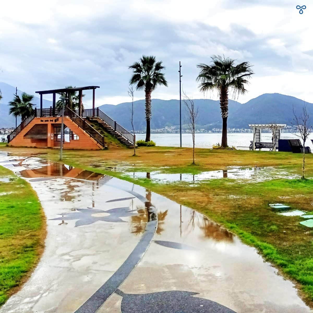 A curved pathway with two palm trees in Fethi Bey Park in Fethiye. The park is waterlogged.