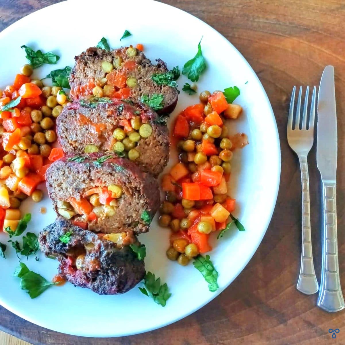 Four slices of Turkish meatloaf served with mixed vegetables. A silver knife and fork is on the right hand side on the table.