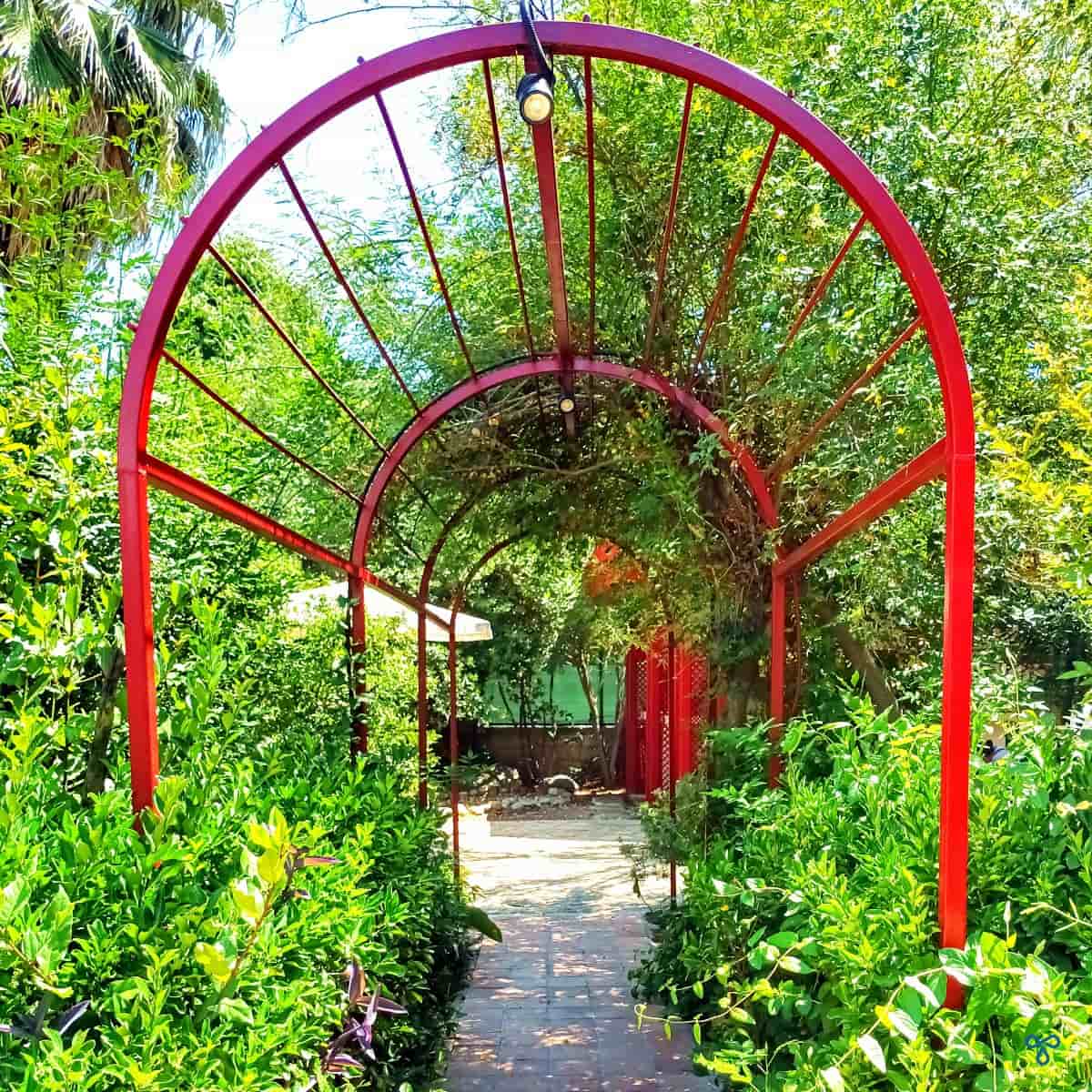 A red metal archway leading through green trees and plants.