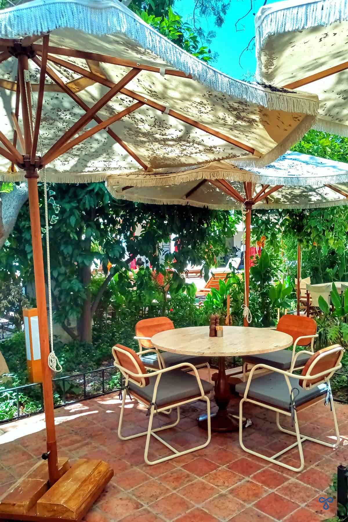A small round table with chairs, shaded by trees and large parasols.
