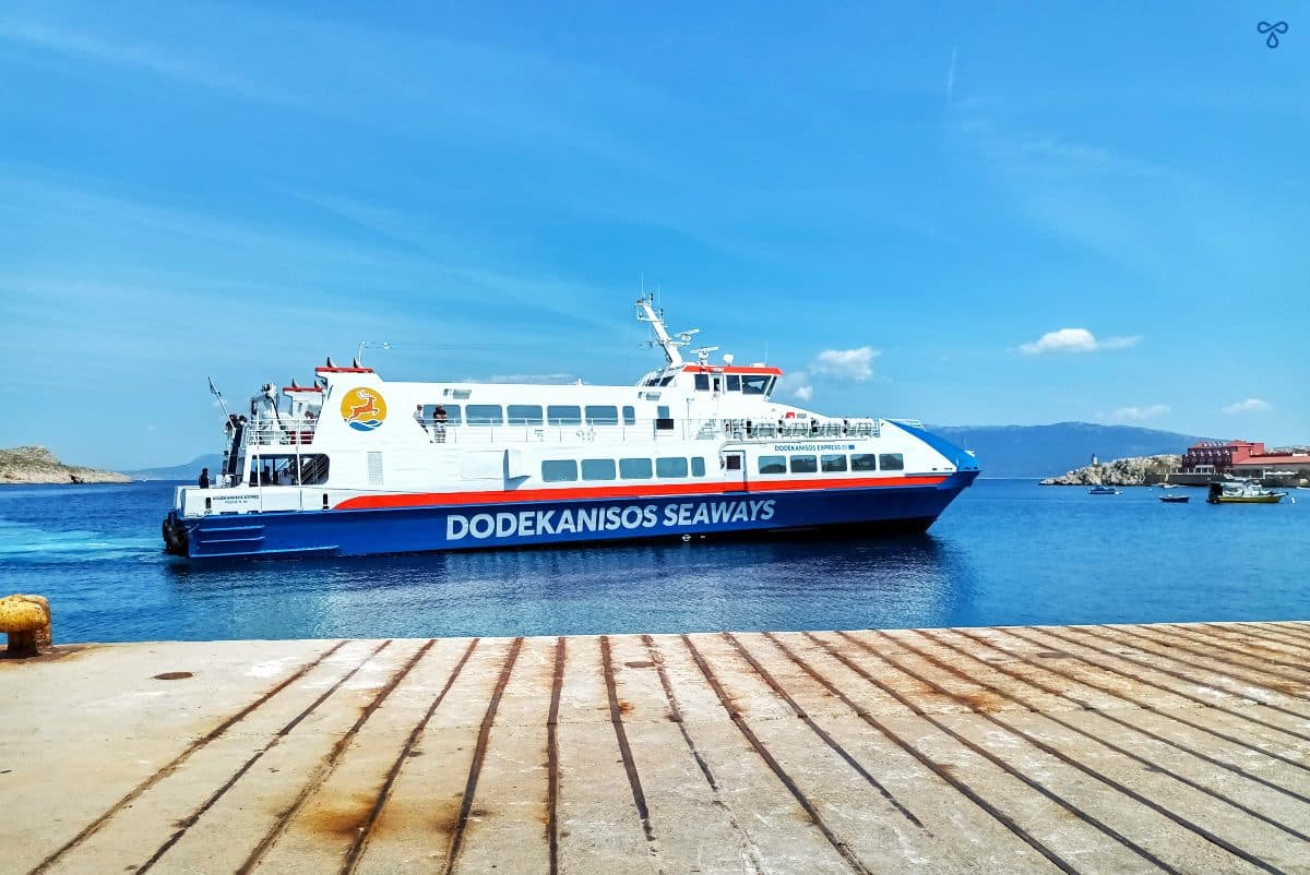A high speed ferry pulling into Halki port. The bottom is blue with Dodekanisos Seaways Written on the side.