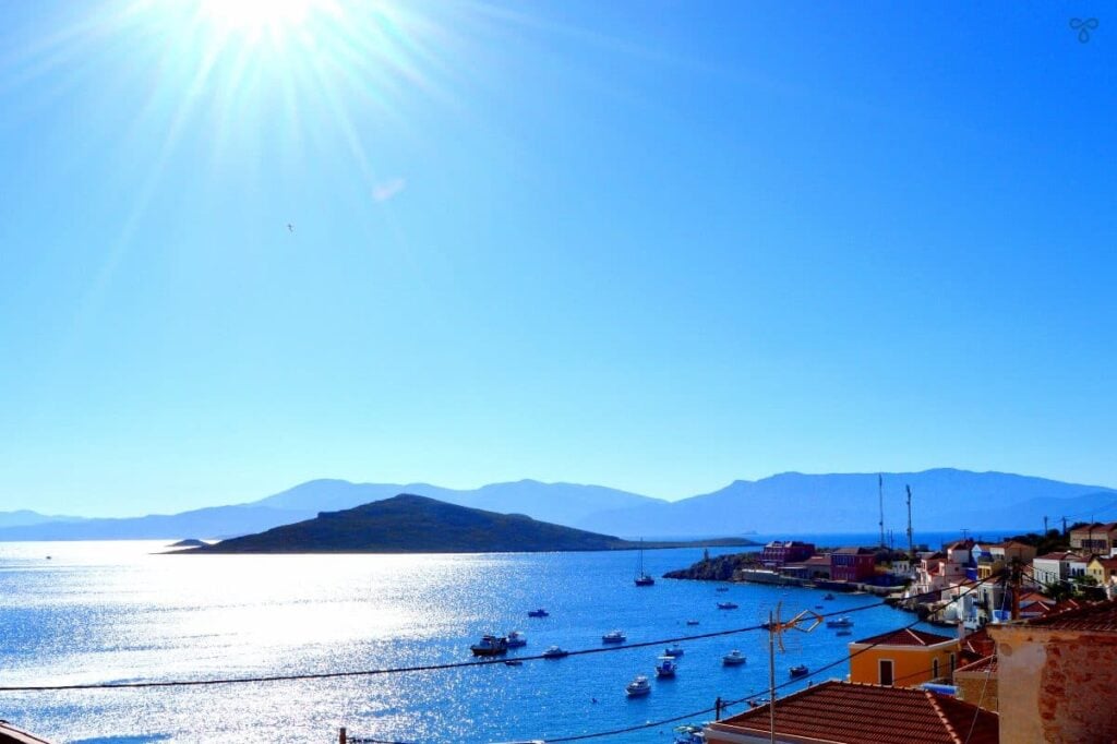 A sea view from Halki island. Small boats are dotted around the harbour and silhouetted islets are visible in the distance.