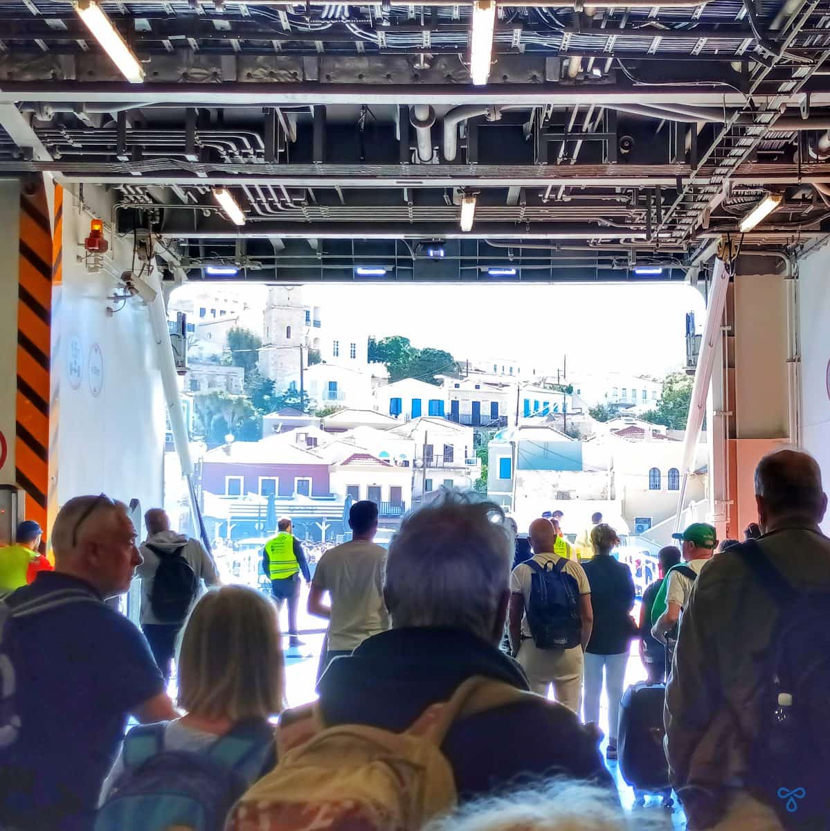 Looking out over a crowd of people disembarking from inside a ferry hold. Halki harbour is visible ahead.