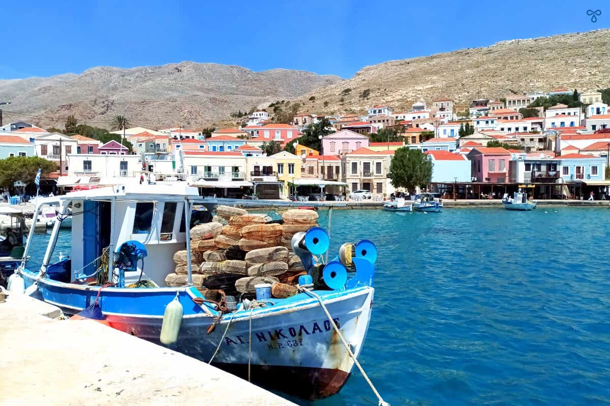 A small fishing boat with doughnut nets piled up on the front. Harbourside buildings are in the background.