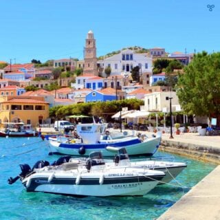 Small boats in Halki harbour with the clock tower rising above the colourful buildings behind