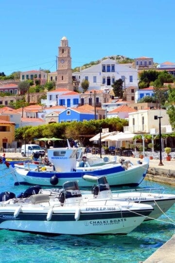 Small boats in Halki harbour with the clock tower rising above the colourful buildings behind