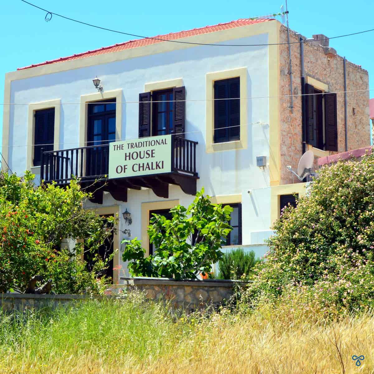 A white-fronted neoclassical house with a sign on the front reading, Traditional House of Halki