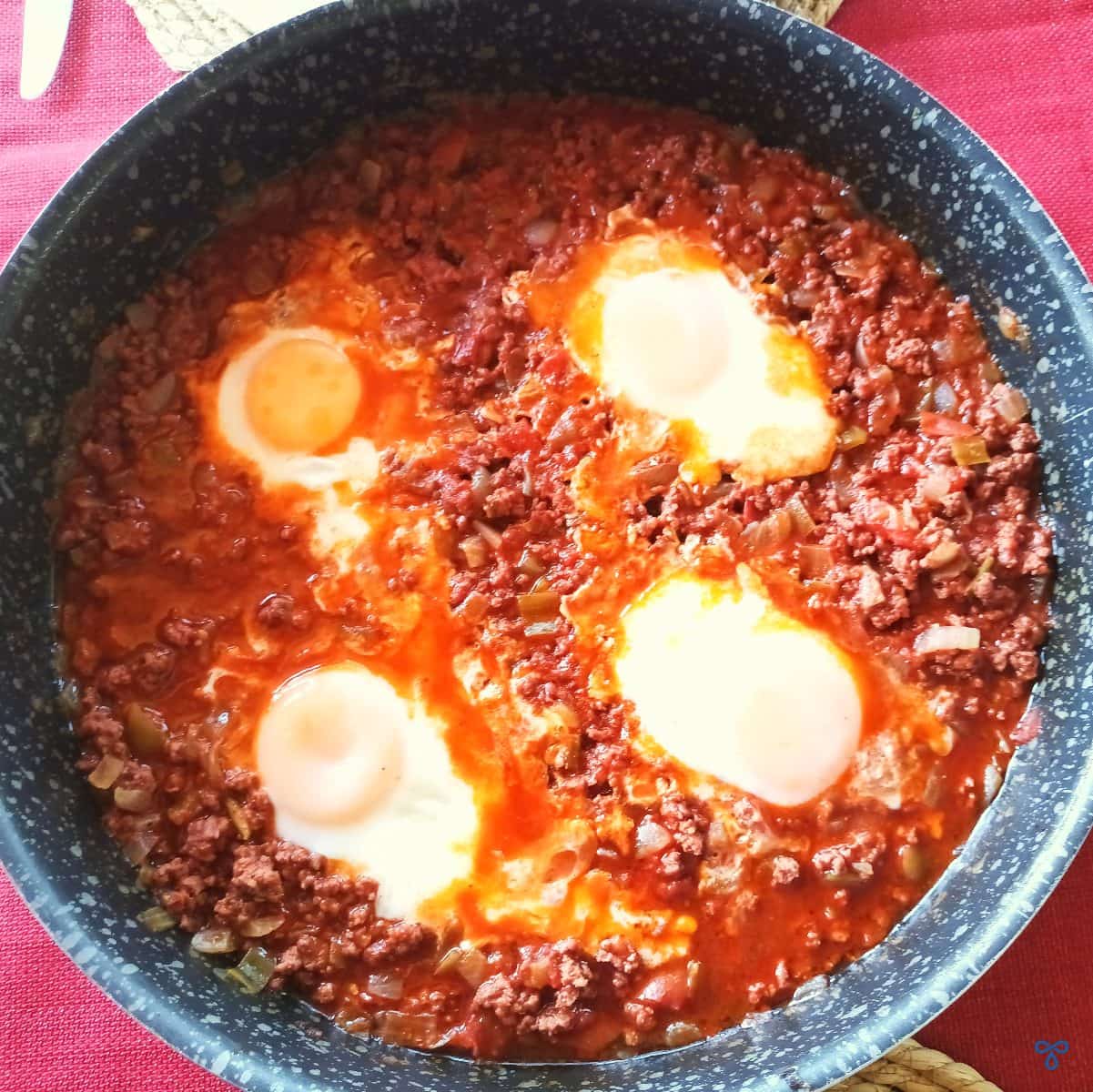 Four eggs poached in minced beef and juices. The photo is taken from above.