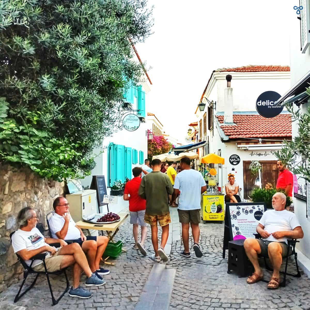 A mediaeval narrow cobbled street in Sığacık, Izmir. Men are sitting either side of the street, chatting and selling fruit.