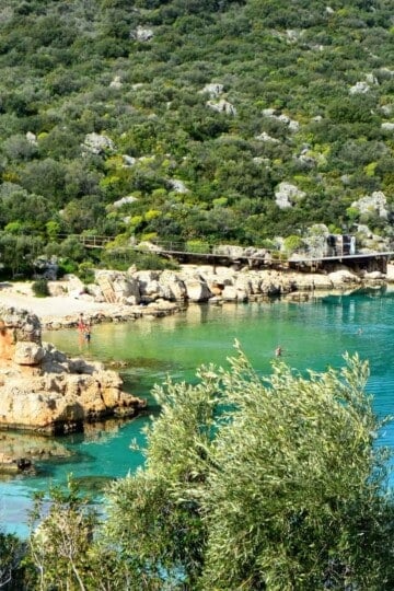 A rocky cove taken from above. A few people are swimming in the water.