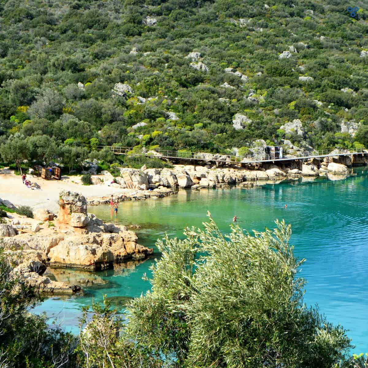 A rocky cove taken from above. A few people are swimming in the water around the peninsula.