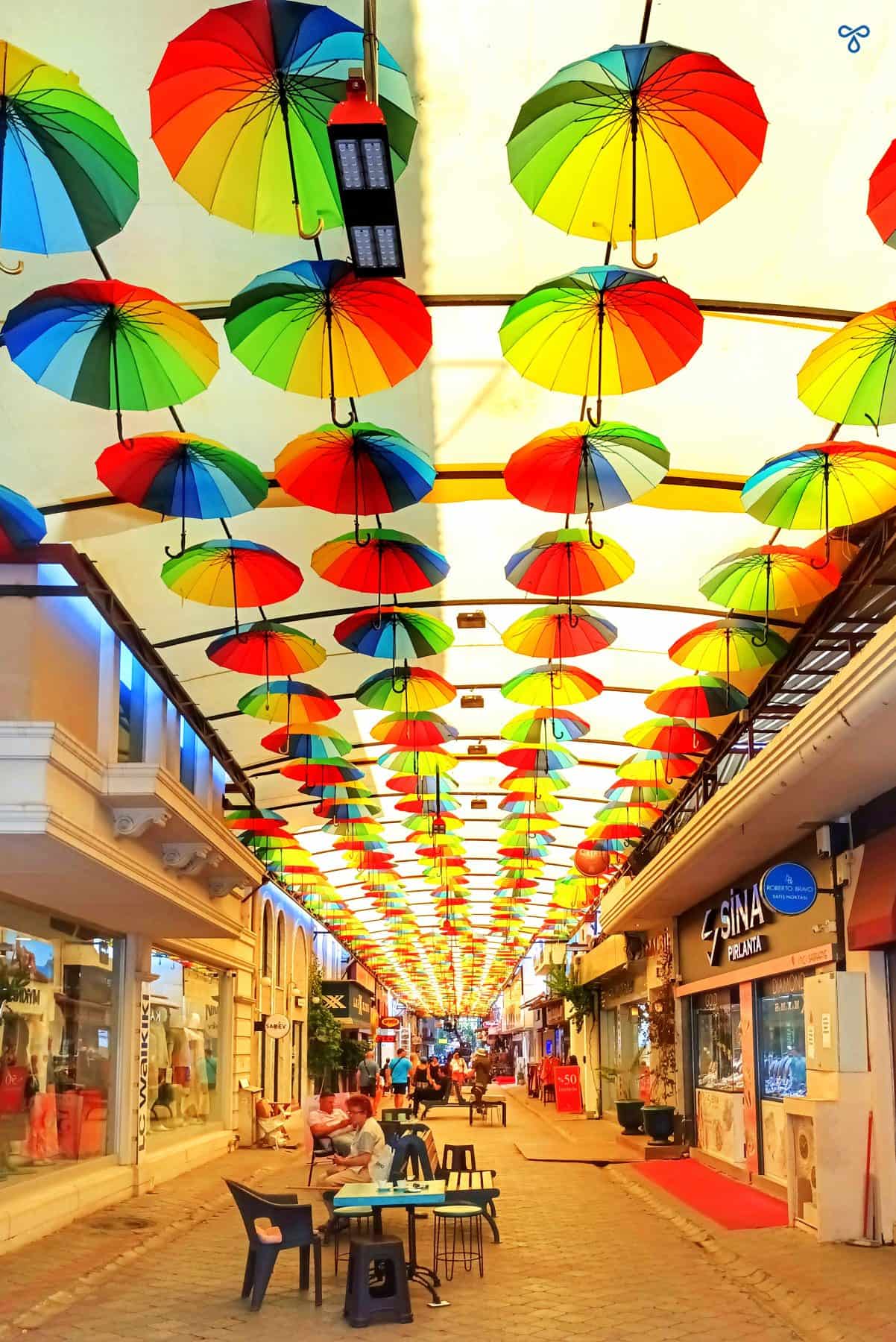 A pedestrianised street in Fethiye. Each side is lined with shops and colourful umbrellas shade the area.