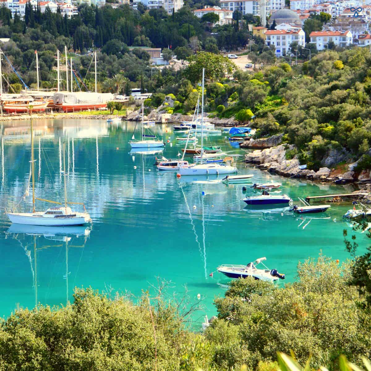A view over clear turquoise sea of the Kaş marina. Fishing boats and yachts are moored along the coast.