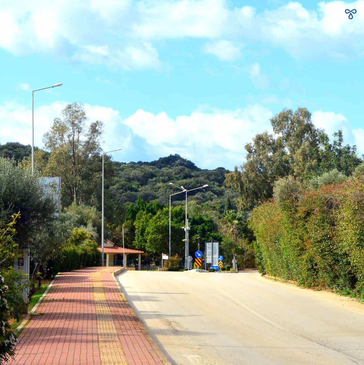 A red pedestrian pavement along a road. A yellow band runs along the pavement for the visually impaired. There's a fork in the road just ahead which marks the start of the Cukurbağ Peninsula loop.