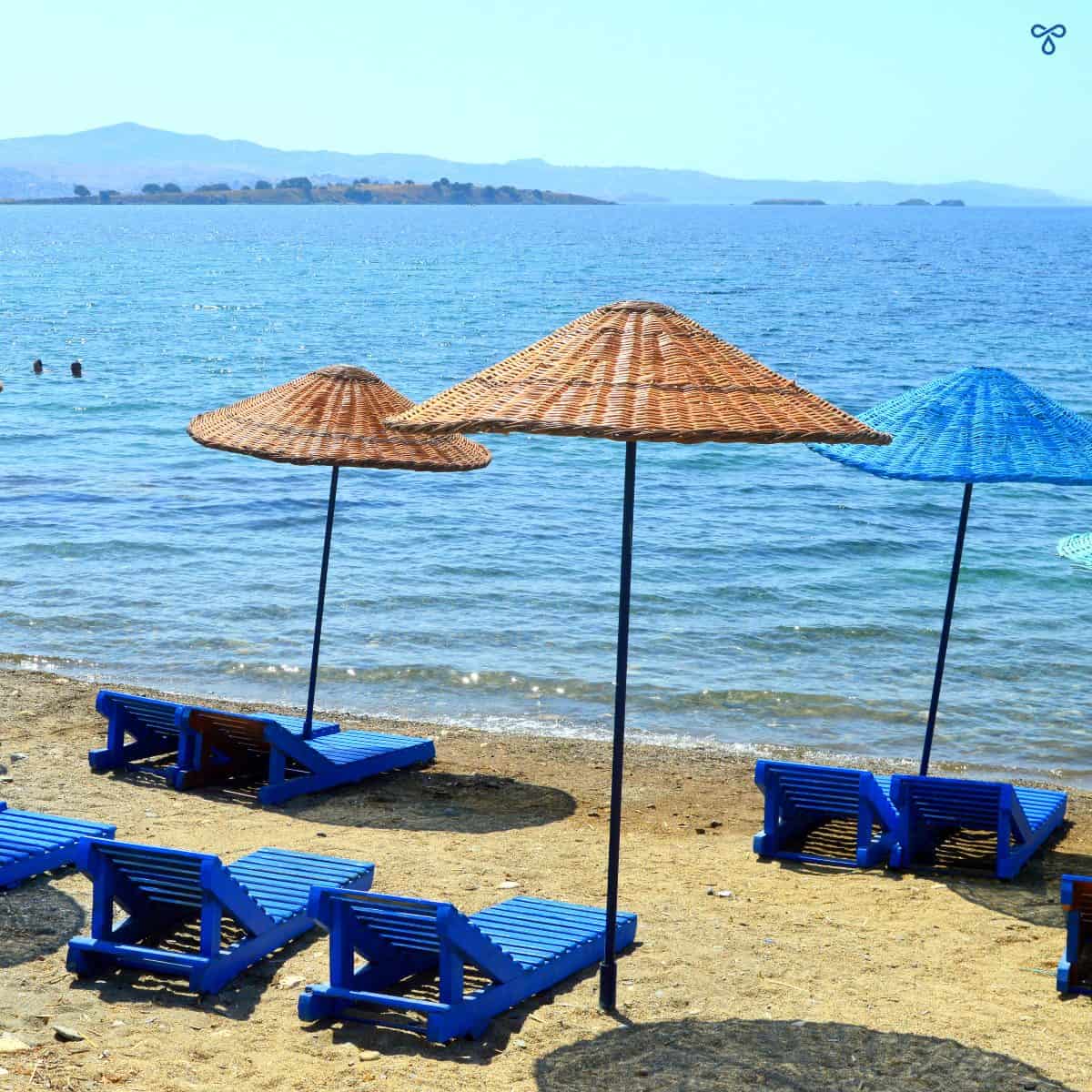 3 rattan sun umbrellas on a beach with blue painted wooden sun loungers.