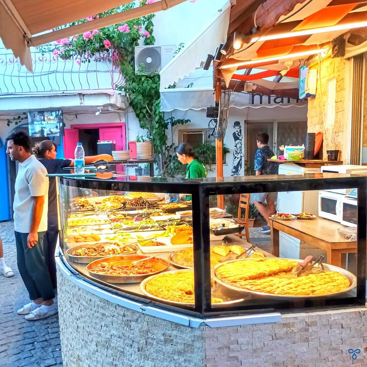 An outdoor glass food display with a waiter stood in front of it.