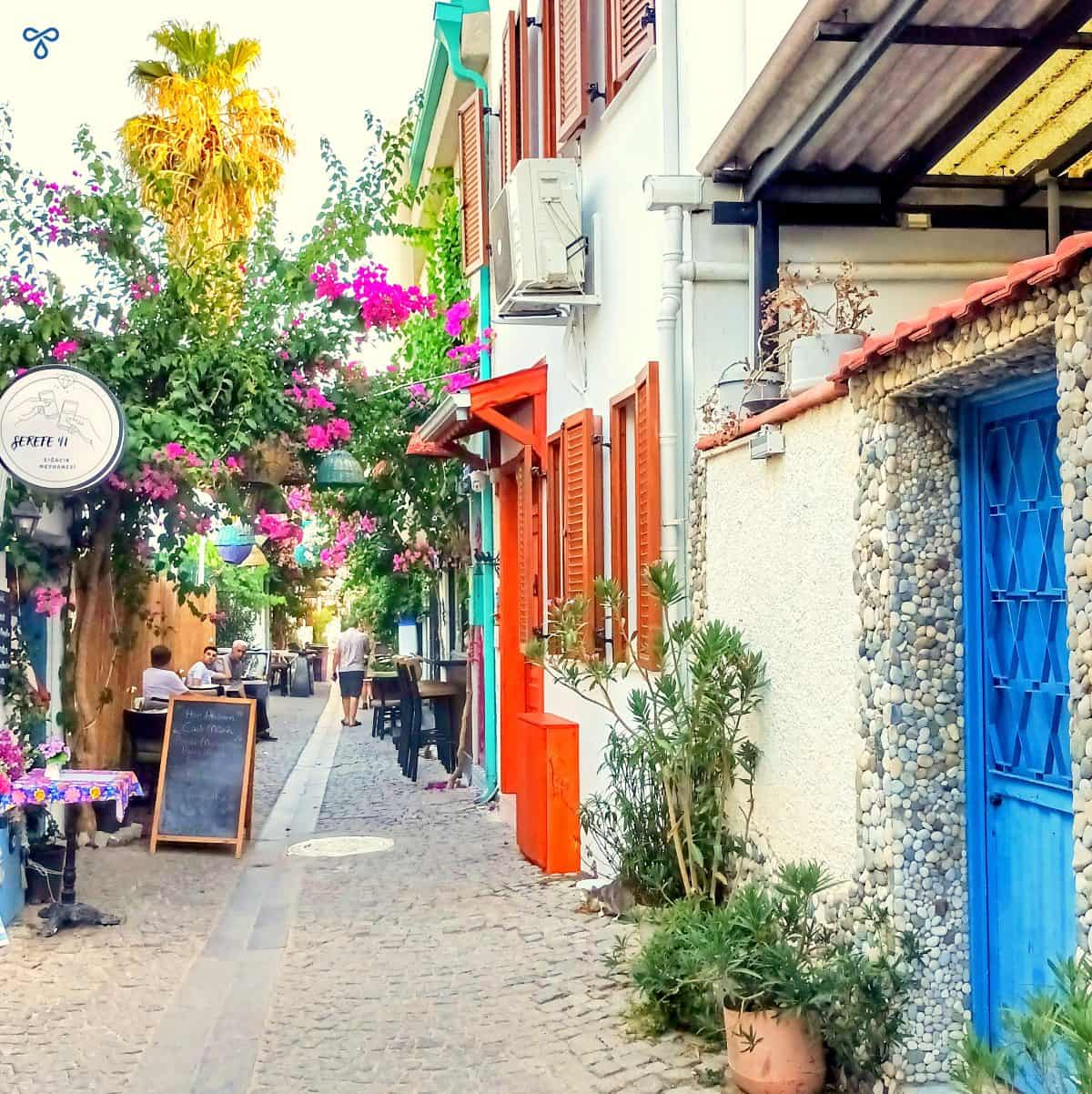A narrow cobbled street of Sığacık. Brightly coloured windows and doors contrast with the whitewashed buildings.