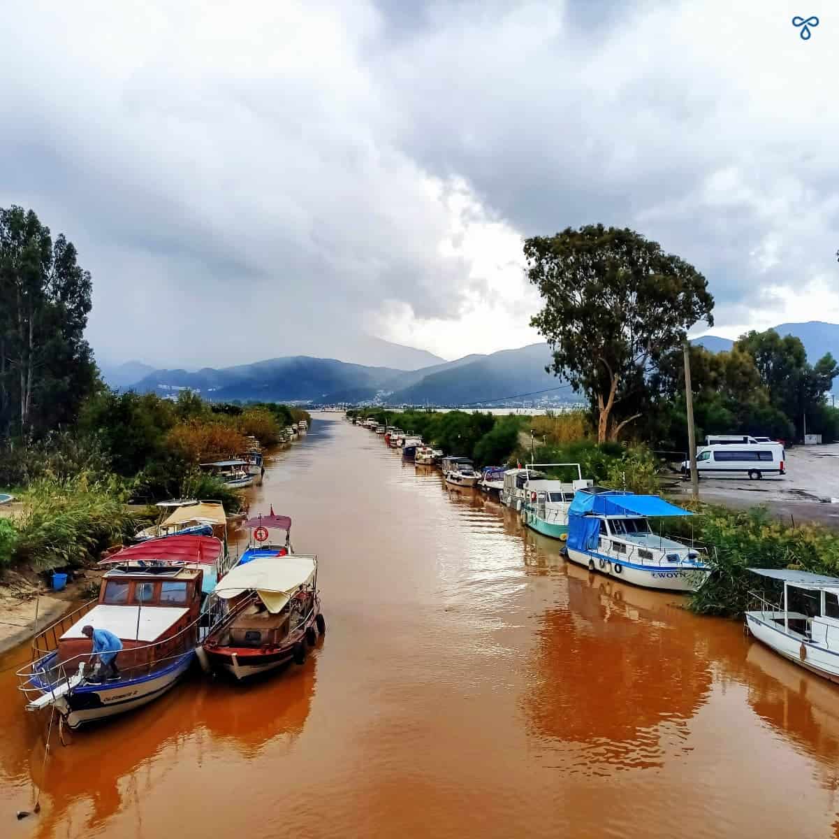 Looking down over a chocolate-coloured canal after a storm. More rain is approaching in the distance and boats line the water's edge.