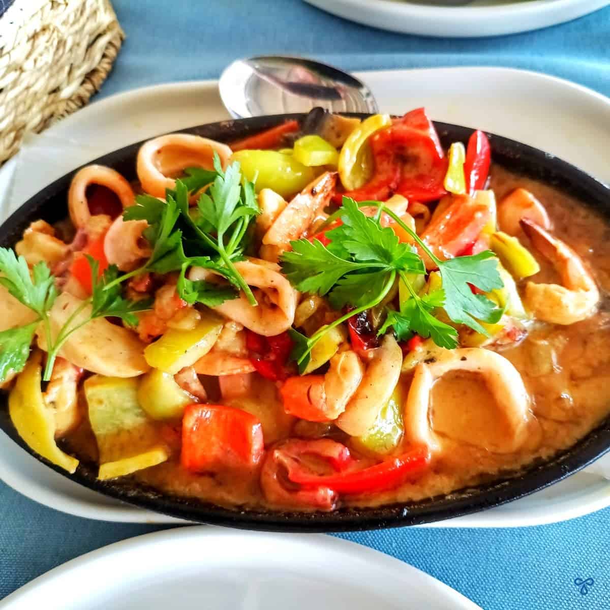 An oval-shaped bowl filled with a creamy seafood stew. Calamari rings and peppers are visible and the dish is topped with fresh parsley.