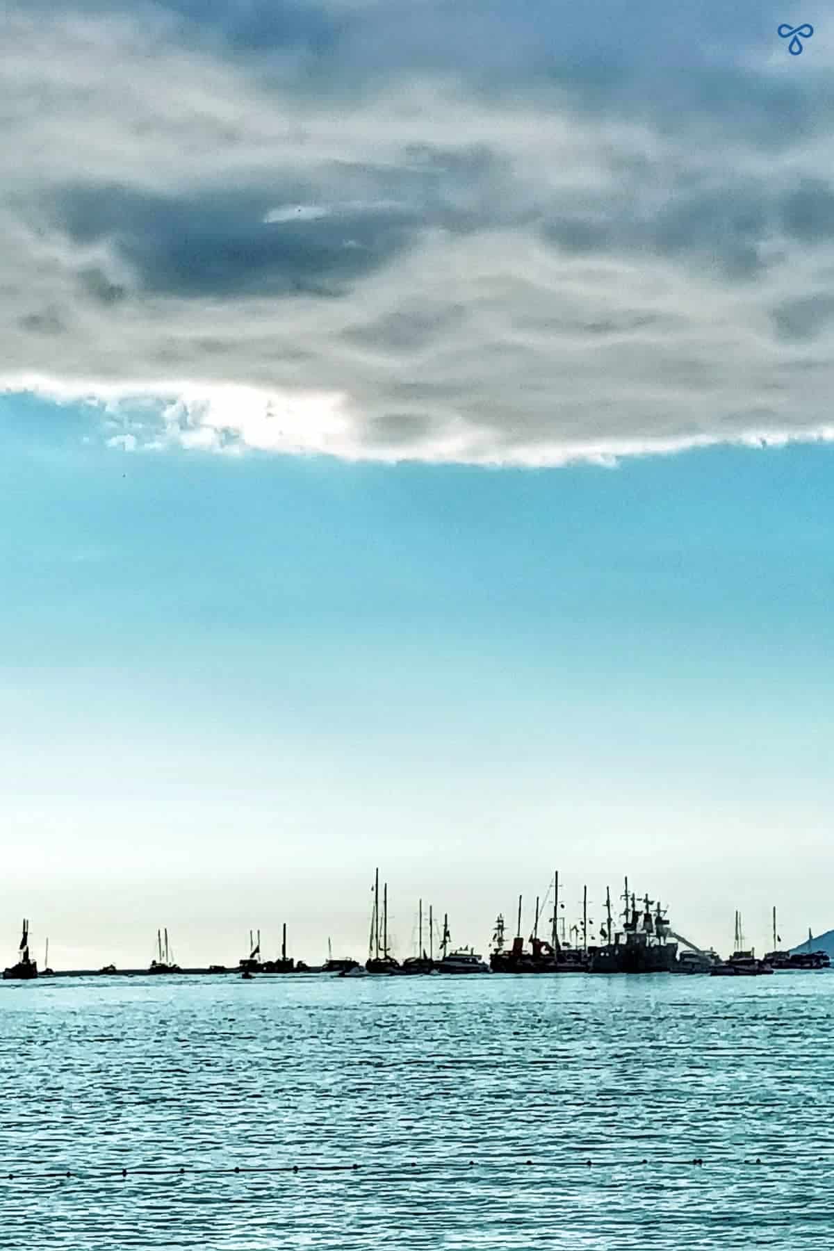Silhouetted boats on the horizon with a cloudy sky above.