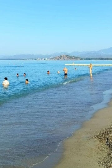 People swimming in a calm sea and a few sunbathing on the beach in Çalış.