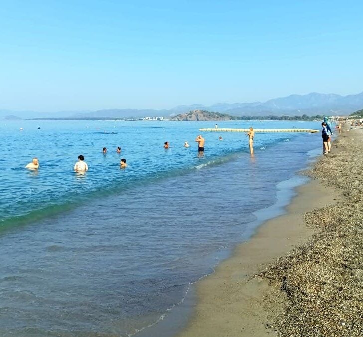 People swimming in a calm sea and a few sunbathing on the beach in Çalış.