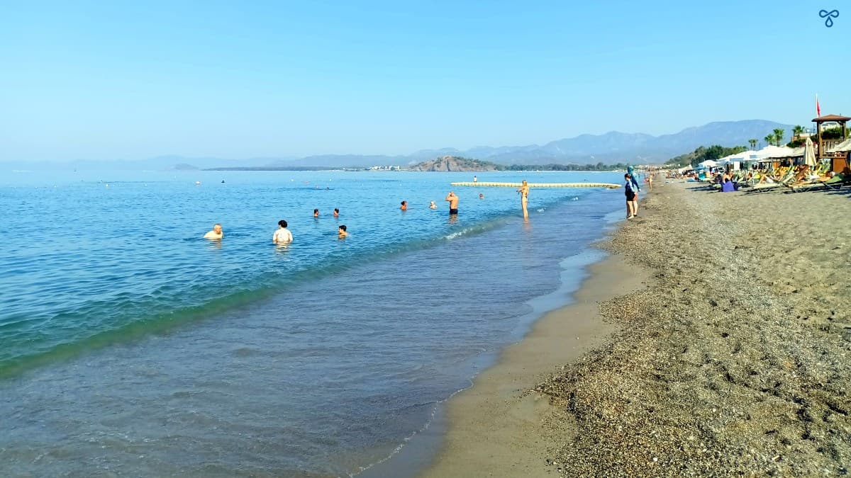 People swimming in a calm sea and a few sunbathers on the beach in Çalış.